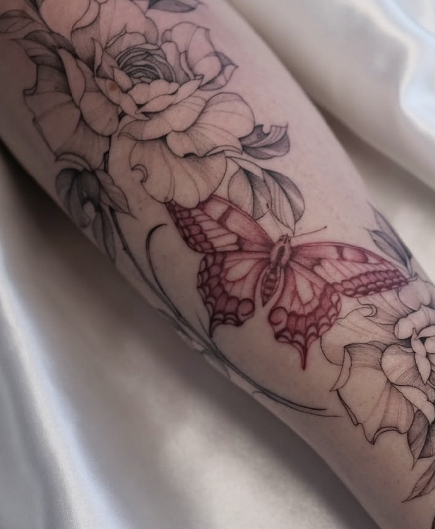 Fineline bloementattoo met een rode vlinder in kleur