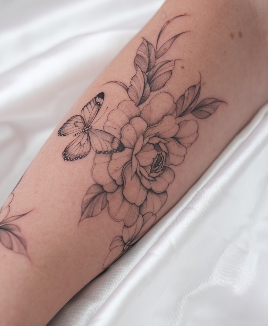 Fineline tattoo met grote bloemen en een vlinder over de onderarm