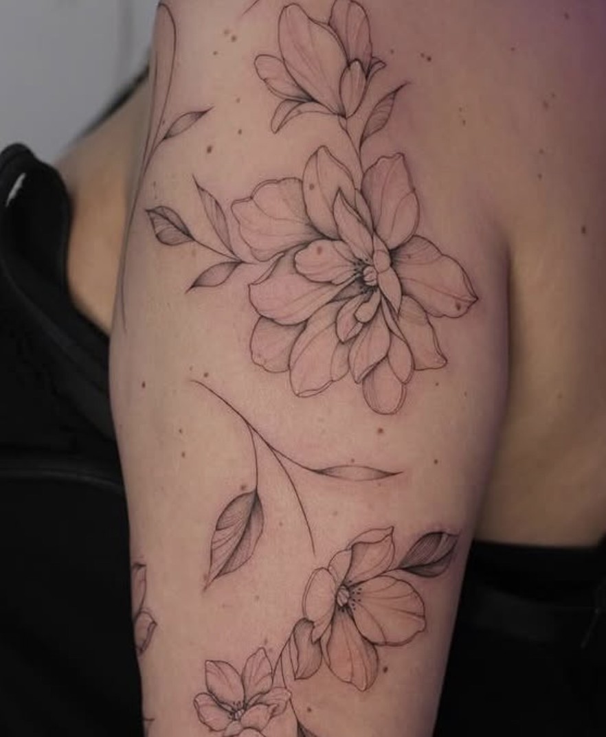 Fineline tattoo van een bloesemtak over de schouder en arm