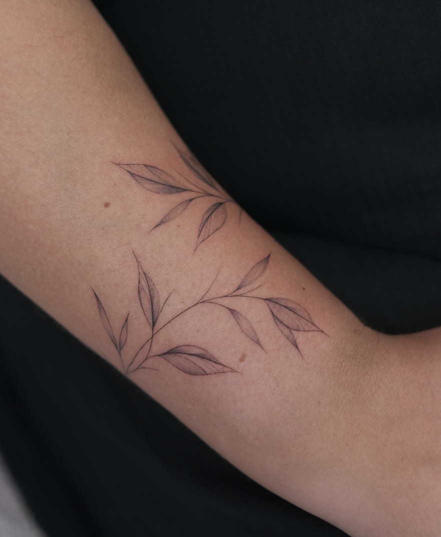 Fineline tattoo van een fijn takje met blaadjes op de arm