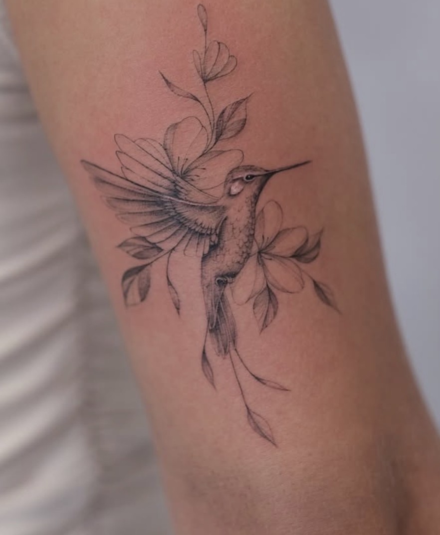 Fineline tattoo van een kolibrie tussen bloemen op de arm