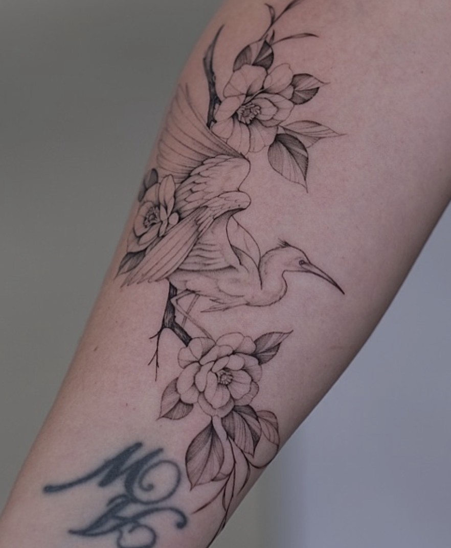 Fineline tattoo van een reiger tussen bloemen op de onderarm