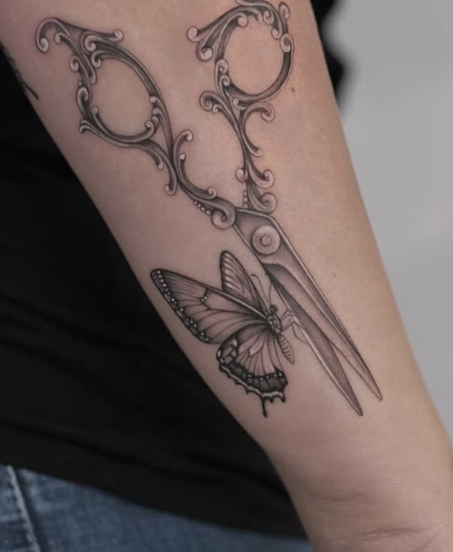 Fineline tattoo van een sierlijke schaar met een vlinder op de arm