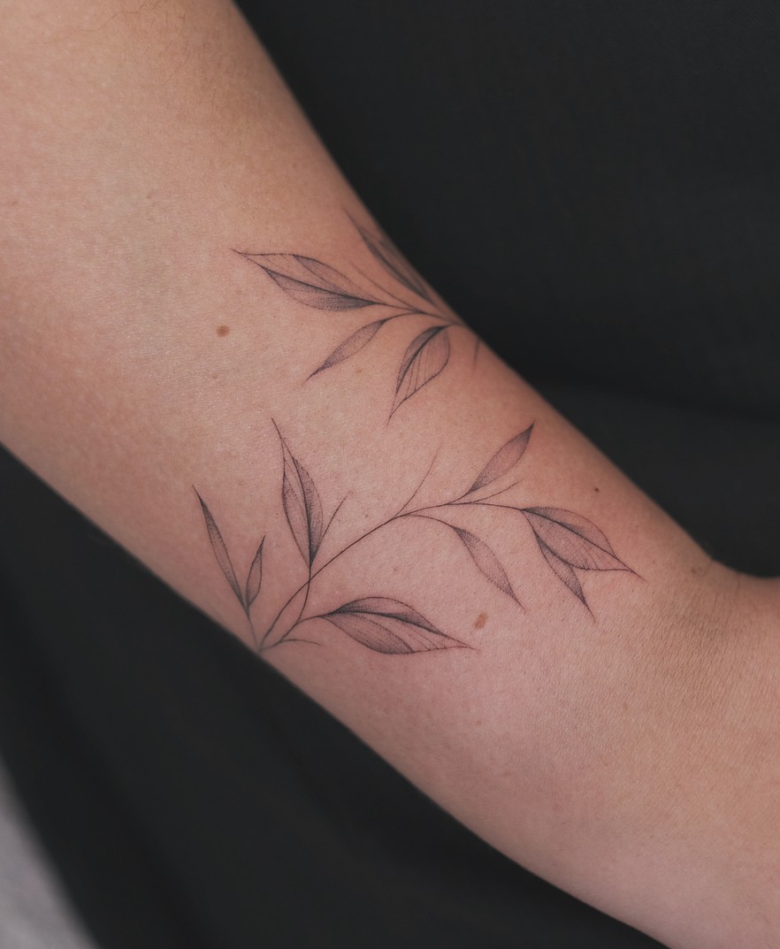 Fineline tattoo van een tak met blaadjes langs de bovenarm