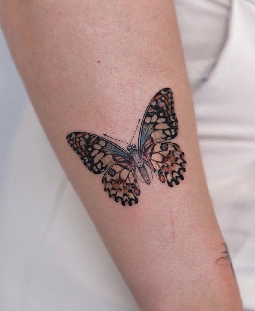 Fineline tattoo van een vlinder in kleur op de onderarm