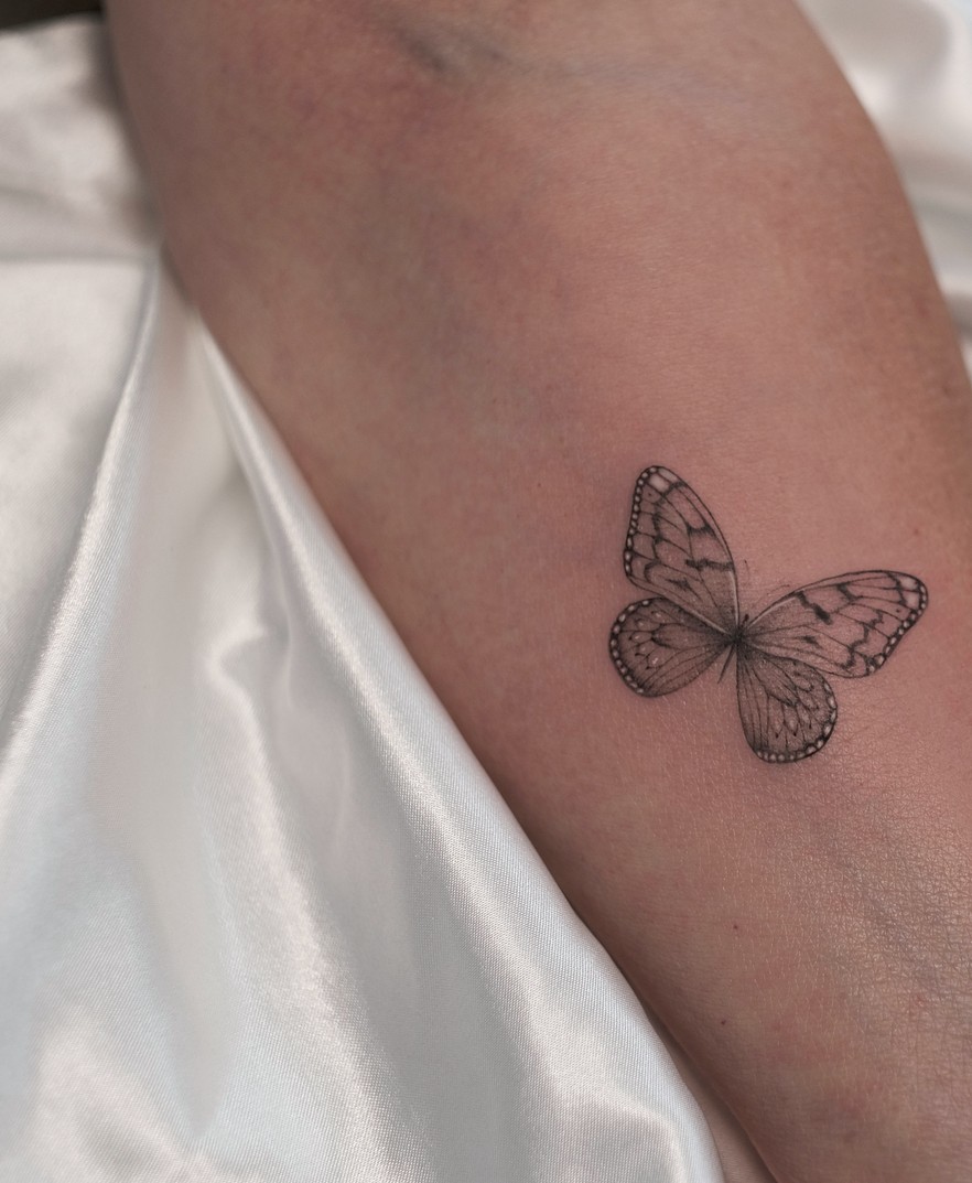 Fineline tattoo van een vlinder op de onderarm