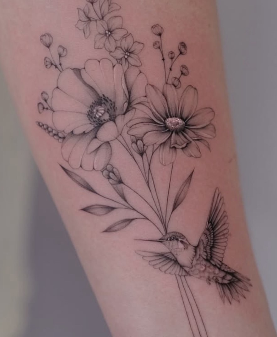 Fineline tattoo van veldbloemen met een kolibrie op de arm