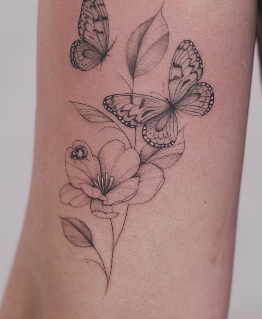 Fineline tattoo van vlinders boven een bloem op de bovenarm
