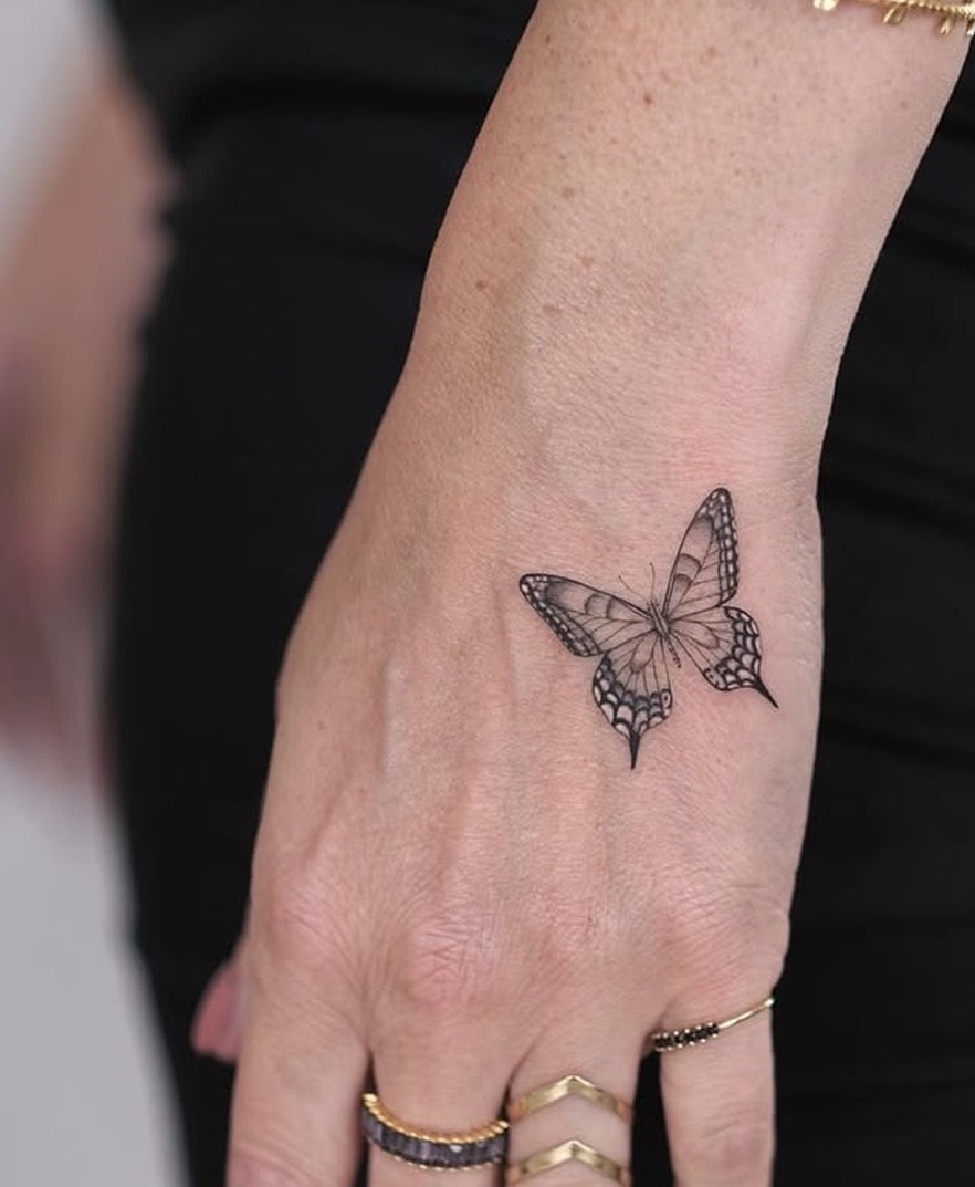 Kleine fineline tattoo van een vlinder op de hand